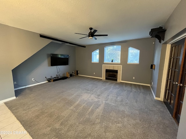 unfurnished living room featuring a tile fireplace, ceiling fan, lofted ceiling, a textured ceiling, and carpet