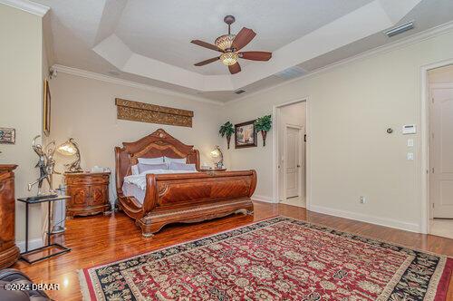 bedroom featuring hardwood / wood-style flooring, ceiling fan, a raised ceiling, and ornamental molding