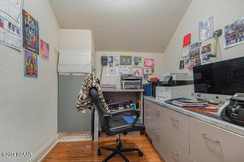 home office with a textured ceiling, vaulted ceiling, and light hardwood / wood-style flooring