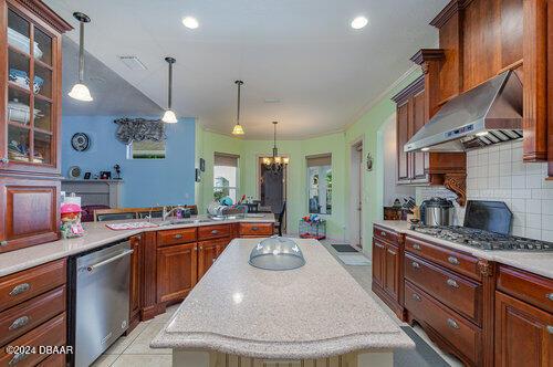 kitchen with exhaust hood, hanging light fixtures, tasteful backsplash, stainless steel appliances, and a chandelier