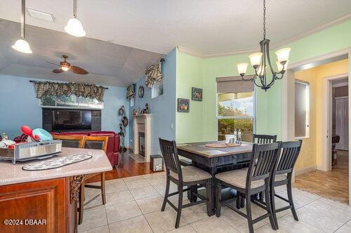 dining room with ceiling fan with notable chandelier, vaulted ceiling, ornamental molding, and light hardwood / wood-style flooring