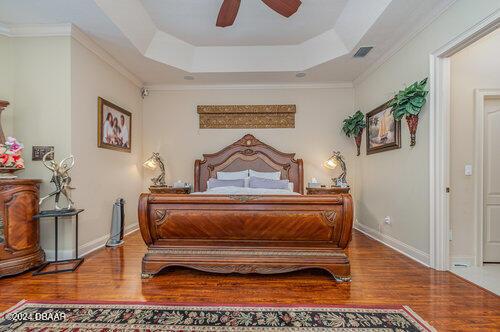 bedroom featuring hardwood / wood-style flooring, ceiling fan, ornamental molding, and a tray ceiling