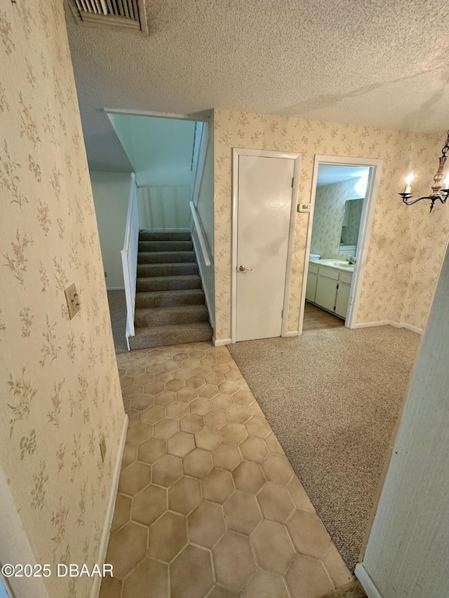 4150 S Atlantic Ave Unit 102B, New Smyrna Beach, FL 32169 - stairs featuring wallpapered walls, a chandelier, a textured ceiling, carpet flooring, and tile patterned flooring