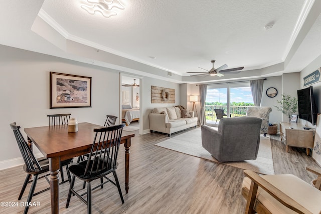 dining room featuring ceiling fan, a textured ceiling, light hardwood / wood-style flooring, and a tray ceiling