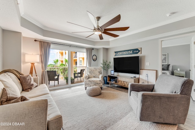 living room with a textured ceiling, ceiling fan, crown molding, and a tray ceiling