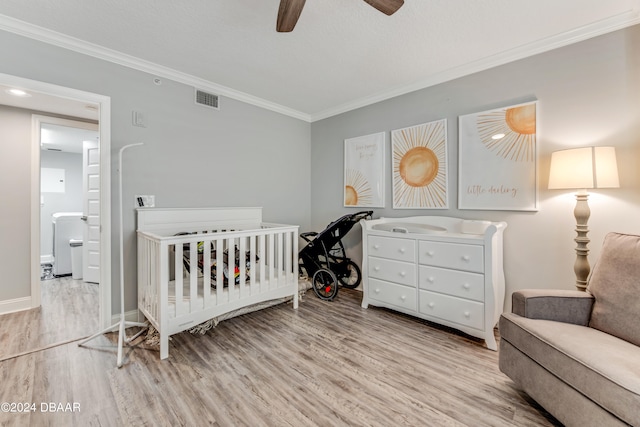 bedroom featuring a crib, light wood-type flooring, ceiling fan, and crown molding