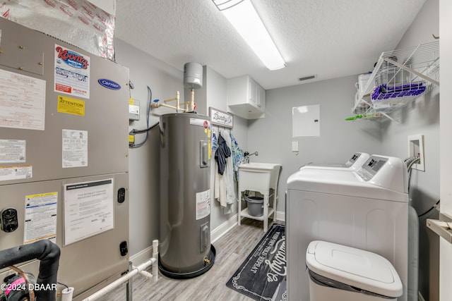 washroom featuring a textured ceiling, heating unit, electric water heater, light wood-type flooring, and washing machine and dryer