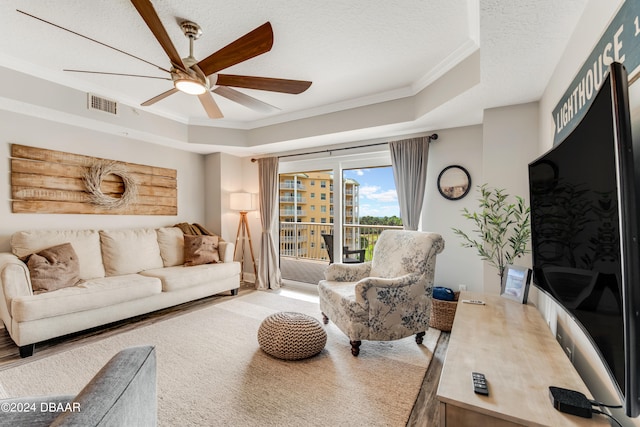 living room with ceiling fan, a textured ceiling, hardwood / wood-style floors, a raised ceiling, and crown molding