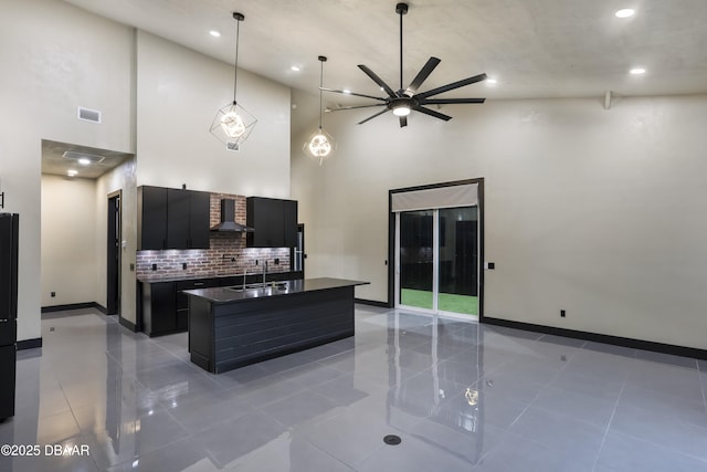 kitchen featuring sink, a towering ceiling, wall chimney exhaust hood, and a center island with sink