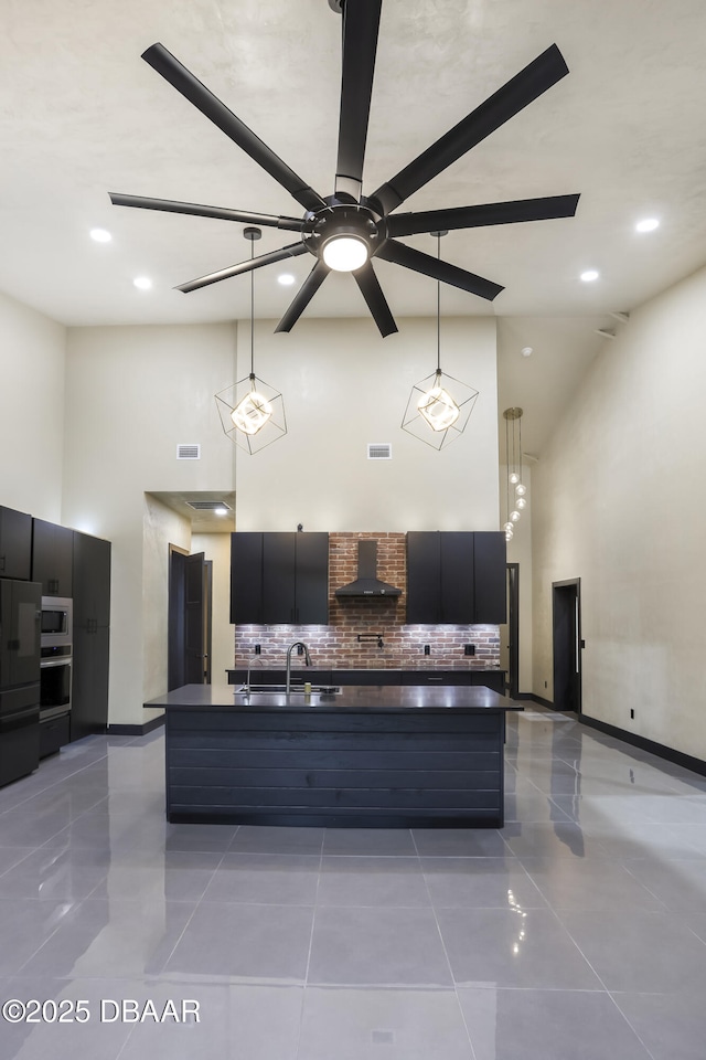 kitchen featuring a high ceiling, sink, wall chimney range hood, and decorative light fixtures