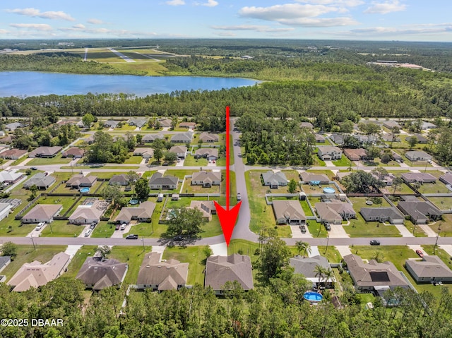view of property location featuring a large body of water, nearby suburban area, and a forest
