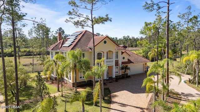 view of home's exterior with solar panels, a chimney, a tiled roof, an attached garage, and decorative driveway