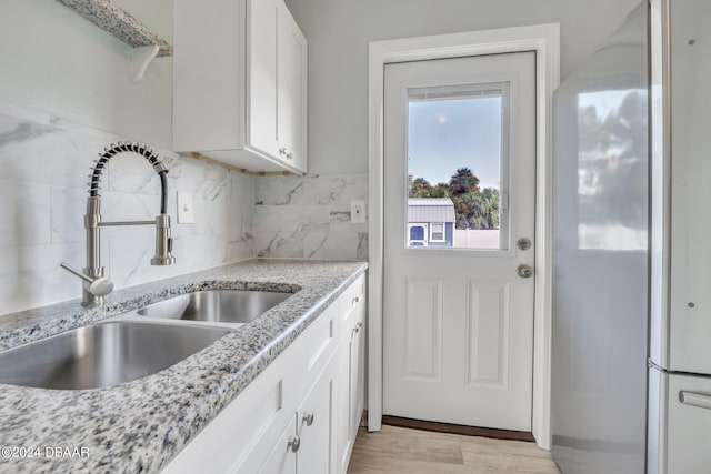 kitchen with light hardwood / wood-style floors, white cabinetry, sink, light stone counters, and decorative backsplash