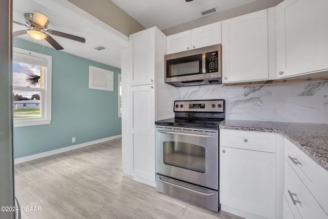 kitchen with tasteful backsplash, light stone counters, light wood-type flooring, appliances with stainless steel finishes, and white cabinets