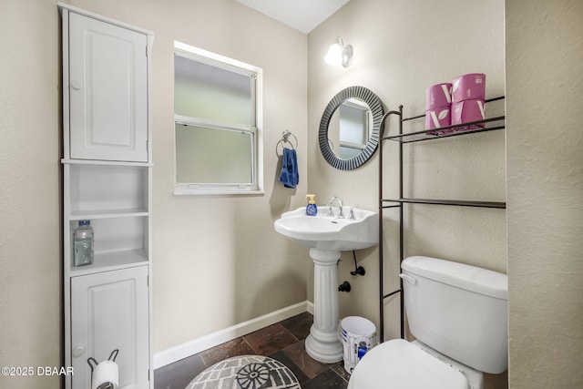 bathroom featuring stone tile floors, baseboards, and toilet