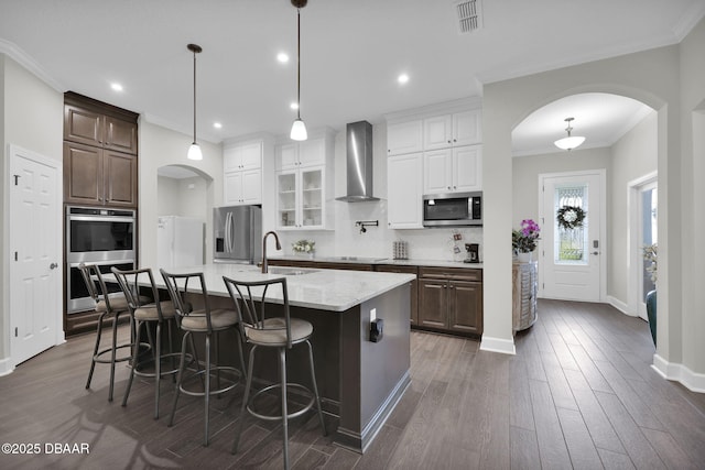 kitchen featuring a sink, stainless steel appliances, arched walkways, and wall chimney range hood