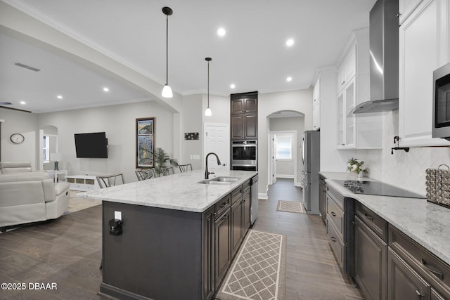 kitchen with visible vents, a sink, arched walkways, appliances with stainless steel finishes, and wall chimney range hood