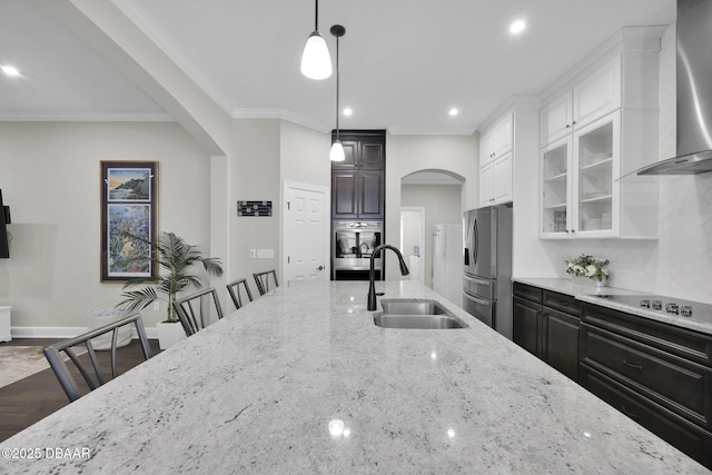 kitchen featuring arched walkways, appliances with stainless steel finishes, wall chimney range hood, and a sink