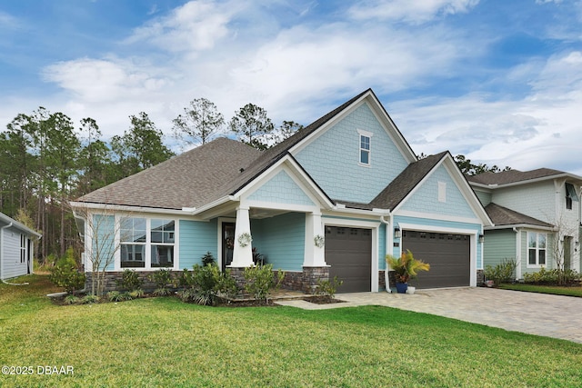 craftsman-style home with decorative driveway, stone siding, roof with shingles, and a front lawn