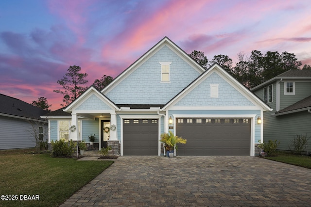 view of front facade featuring a front lawn, decorative driveway, a garage, and stone siding