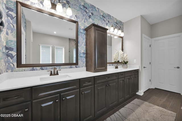 full bath featuring double vanity, wood finished floors, wallpapered walls, and a sink