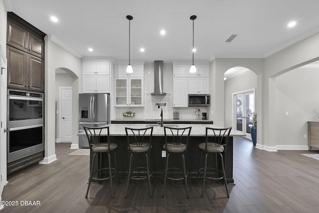 kitchen featuring tasteful backsplash, visible vents, wall chimney range hood, appliances with stainless steel finishes, and arched walkways