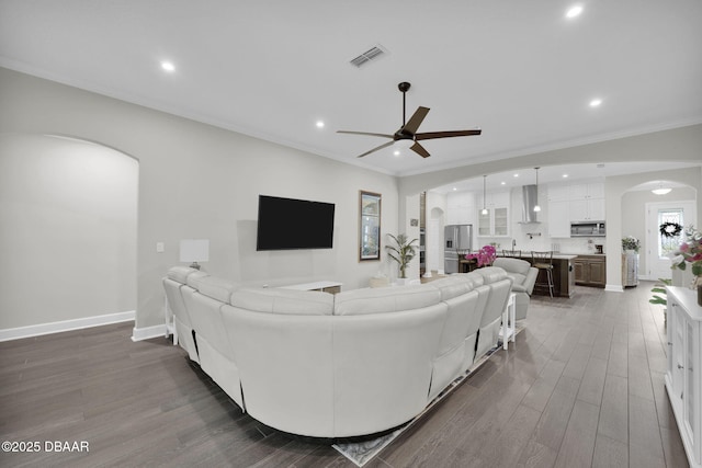 living area featuring visible vents, crown molding, baseboards, dark wood finished floors, and arched walkways