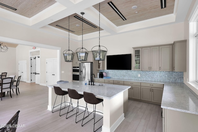 kitchen featuring a kitchen bar, gray cabinetry, a sink, stainless steel appliances, and decorative backsplash