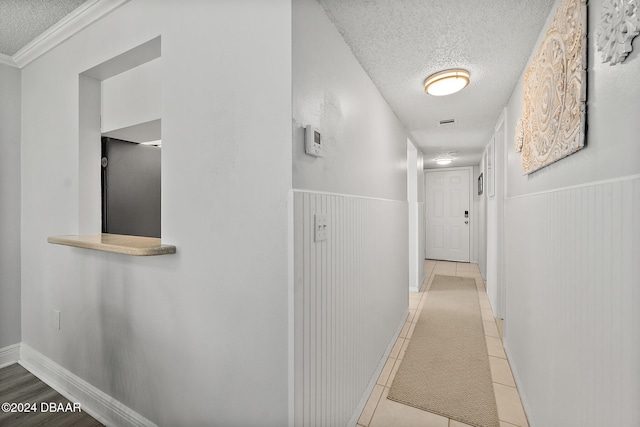 hall with crown molding, wooden walls, light tile patterned floors, and a textured ceiling