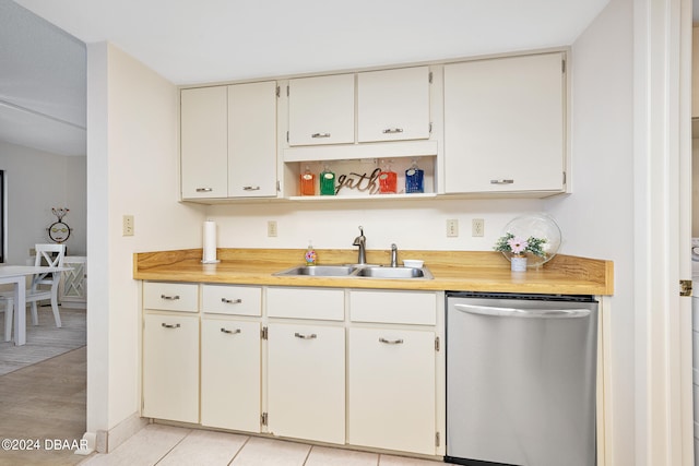 kitchen with stainless steel dishwasher, light tile patterned floors, sink, and white cabinets