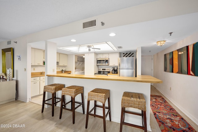 kitchen with a kitchen bar, stainless steel appliances, kitchen peninsula, white cabinetry, and light hardwood / wood-style flooring