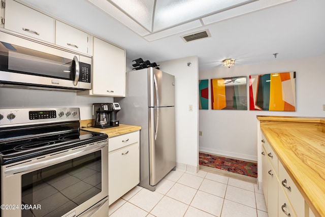 kitchen with stainless steel appliances, wooden counters, white cabinetry, and light tile patterned floors