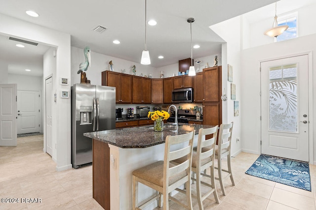 kitchen featuring a kitchen bar, appliances with stainless steel finishes, a center island with sink, hanging light fixtures, and light tile patterned flooring