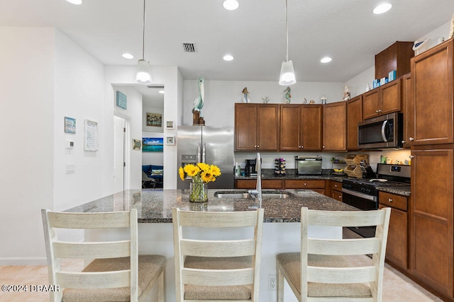 kitchen featuring a breakfast bar area, a kitchen island with sink, pendant lighting, and appliances with stainless steel finishes