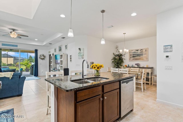 kitchen with dishwasher, sink, dark stone counters, a kitchen island with sink, and ceiling fan with notable chandelier