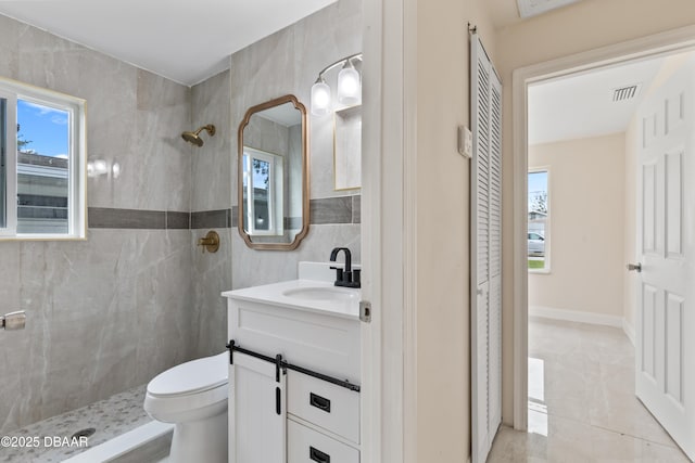 full bathroom featuring vanity, a tile shower, visible vents, and tile walls