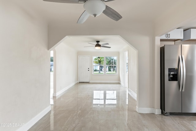 interior space with arched walkways, marble finish floor, a ceiling fan, and baseboards