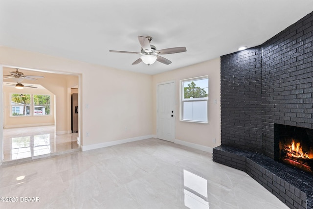 unfurnished living room with a ceiling fan, a wealth of natural light, a brick fireplace, and baseboards