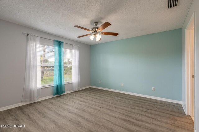 empty room featuring ceiling fan, wood finished floors, a textured ceiling, and plenty of natural light