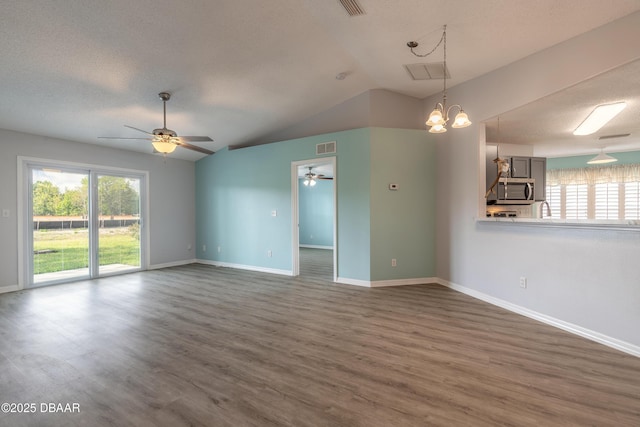 unfurnished living room with plenty of natural light, vaulted ceiling, dark wood-type flooring, and ceiling fan with notable chandelier