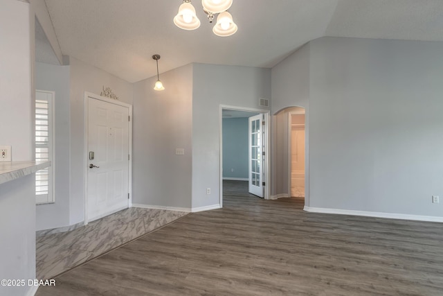 foyer entrance featuring vaulted ceiling, wood finished floors, arched walkways, baseboards, and a chandelier