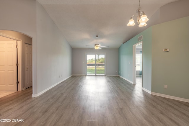 unfurnished living room with arched walkways, vaulted ceiling, visible vents, ceiling fan with notable chandelier, and wood finished floors