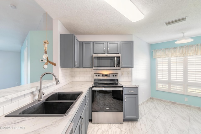 kitchen with stainless steel appliances, visible vents, gray cabinets, a sink, and decorative backsplash
