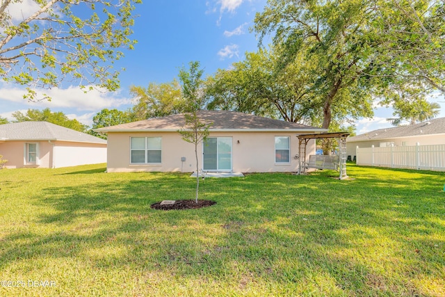 back of house featuring a lawn, stucco siding, and fence