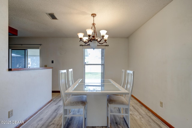 unfurnished dining area with a chandelier, a textured ceiling, and light wood-type flooring