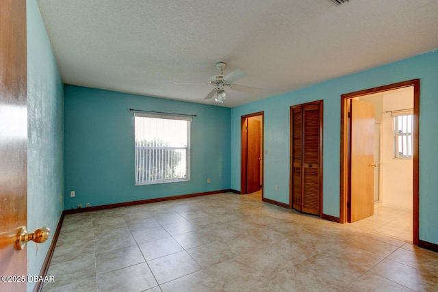 unfurnished bedroom with ceiling fan, light tile patterned floors, ensuite bathroom, and a textured ceiling