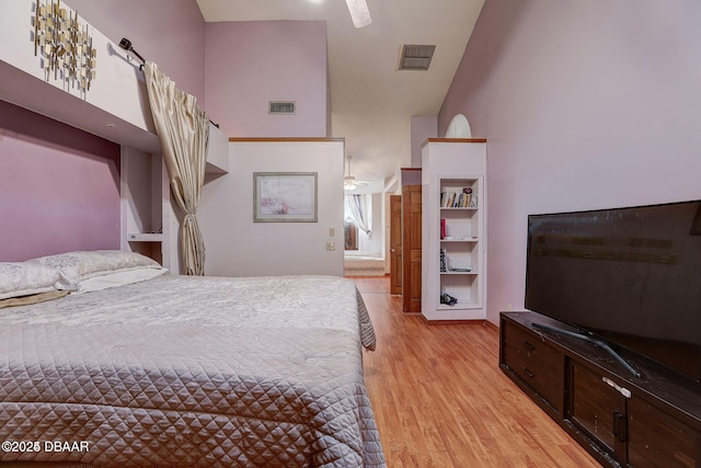 bedroom with light wood-style floors, visible vents, high vaulted ceiling, and ensuite bath