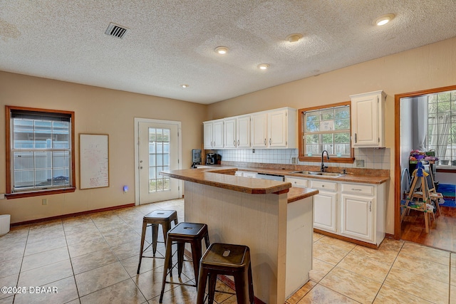 kitchen featuring a breakfast bar area, visible vents, white cabinets, a kitchen island, and a sink