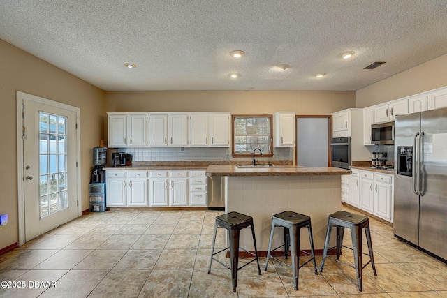 kitchen with stainless steel appliances, visible vents, white cabinetry, a sink, and a kitchen island