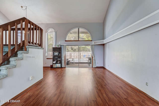 unfurnished living room featuring high vaulted ceiling, stairway, wood finished floors, and baseboards